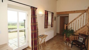 A spacious room with a large sliding glass door leading to a garden, a wooden staircase, and a small table with a chair. - Spring Cottage-E3846 (Kirk Ireton, near Matlock)