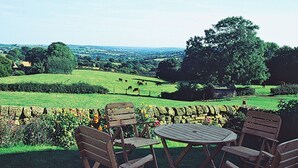 A patio with wooden furniture overlooking a green landscape with cows and trees. - Spring Cottage-E3846 (Kirk Ireton, near Matlock)