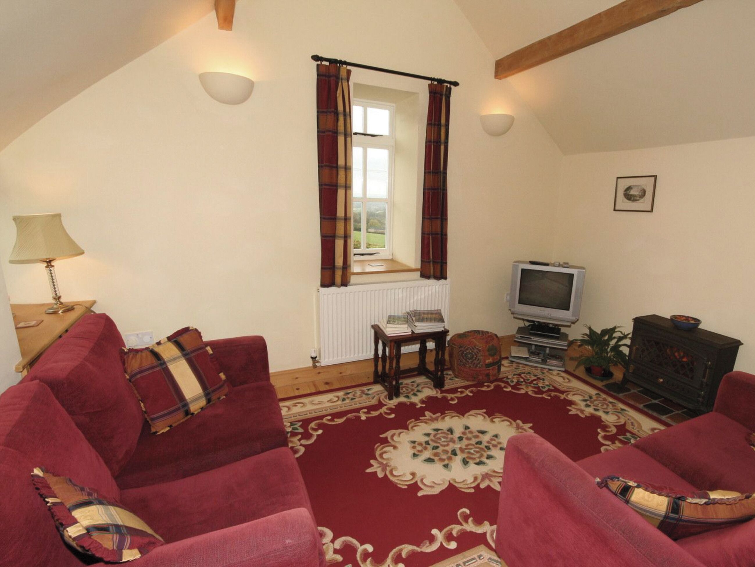 Una sala de estar acogedora con un sofá rojo, televisión, chimenea y una ventana con cortinas.