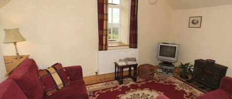 Una sala de estar acogedora con un sofá rojo, televisión, chimenea y una ventana con cortinas.