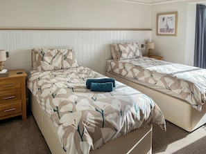 A bedroom with two beds, each with a patterned bedspread, a bedside table with a lamp, and a wall-mounted picture. - 3 bedroom accommodation in Bittaford, near Ivybridge (Bittaford, near Ivybridge)