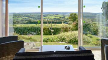 A room with a large sliding glass door leading to a garden. There is a table with a book and a remote control on it.