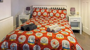 Un lit recouvert d’une couvre-lit à motifs rouges et blancs, deux serviettes enroulées et deux tables de chevet avec des lampes.