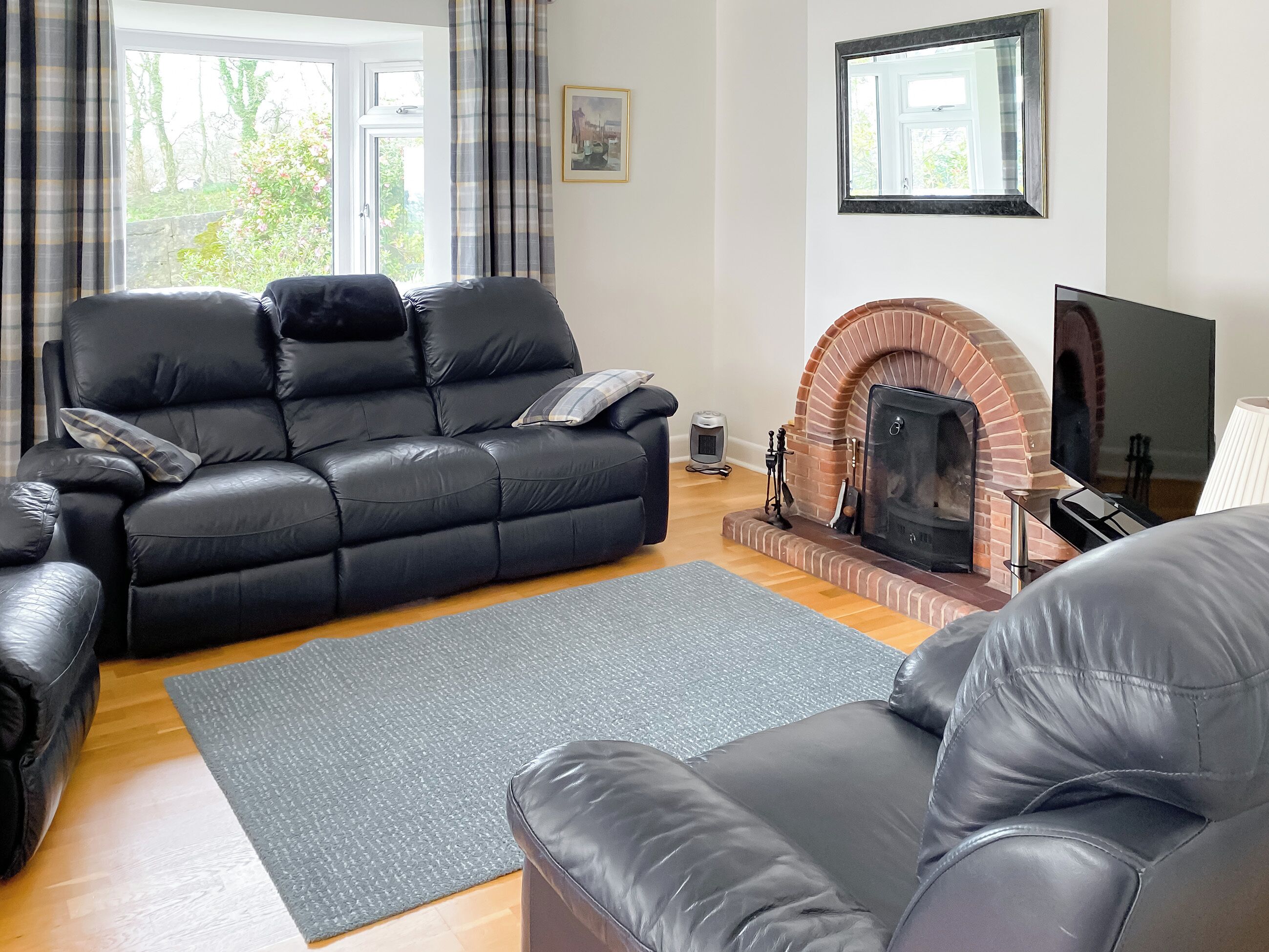 A modern living room with a black leather sofa, a grey rug, a brick fireplace, and a television.