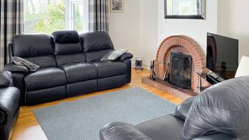 A modern living room with a black leather sofa, a grey rug, a brick fireplace, and a television.