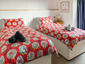 A hotel room with two beds, each with a red bedspread featuring Christmas-themed illustrations. There is a nightstand with a lamp and a framed picture on the wall. - 3 bedroom accommodation in Bittaford, near Ivybridge (Bittaford, near Ivybridge)