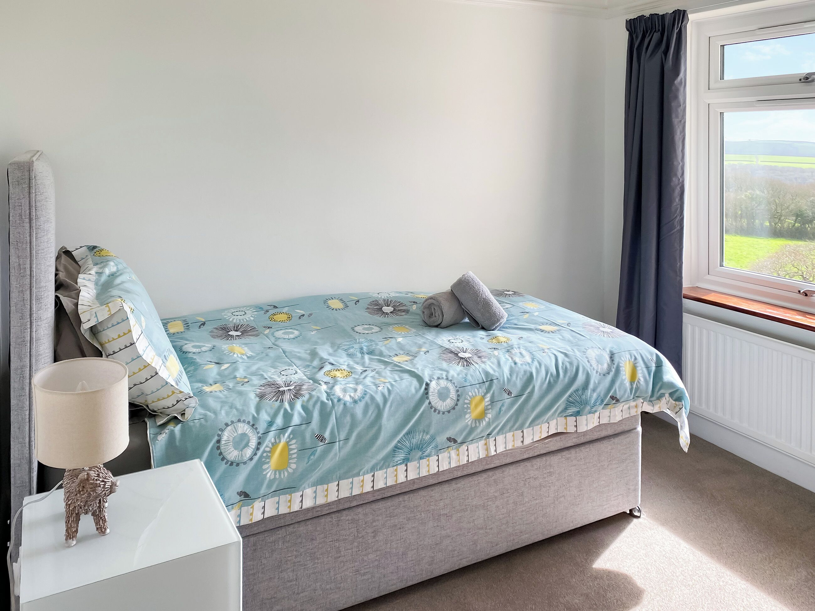 A bedroom with a bed, a nightstand, a lamp, and a window with curtains.