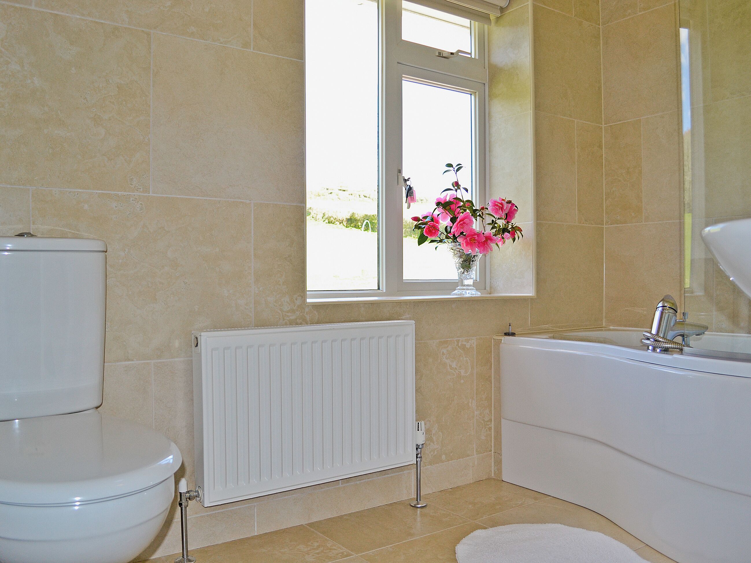 Une salle de bain comprenant des toilettes, un radiateur, une fenêtre avec un vase de fleurs et une baignoire.