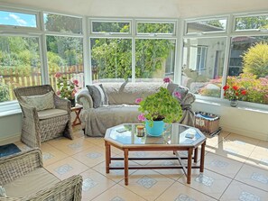 A conservatory with a sofa, chairs, a table, and potted plants.