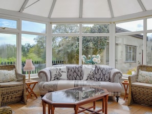 A conservatory with a sofa, two wicker chairs, a glass-top table, and a lamp.