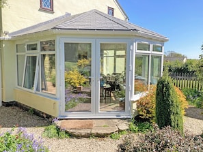 A conservatory with a tiled roof, large glass doors, and a garden view.