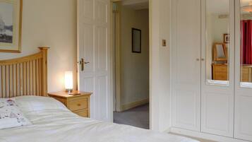 A bedroom with a bed, bedside table, lamp, wardrobe, and a door leading to another room.