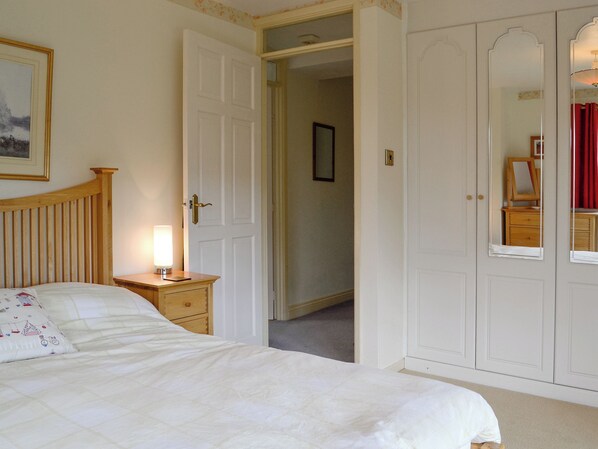 A bedroom with a bed, bedside table, lamp, wardrobe, and a door leading to another room.