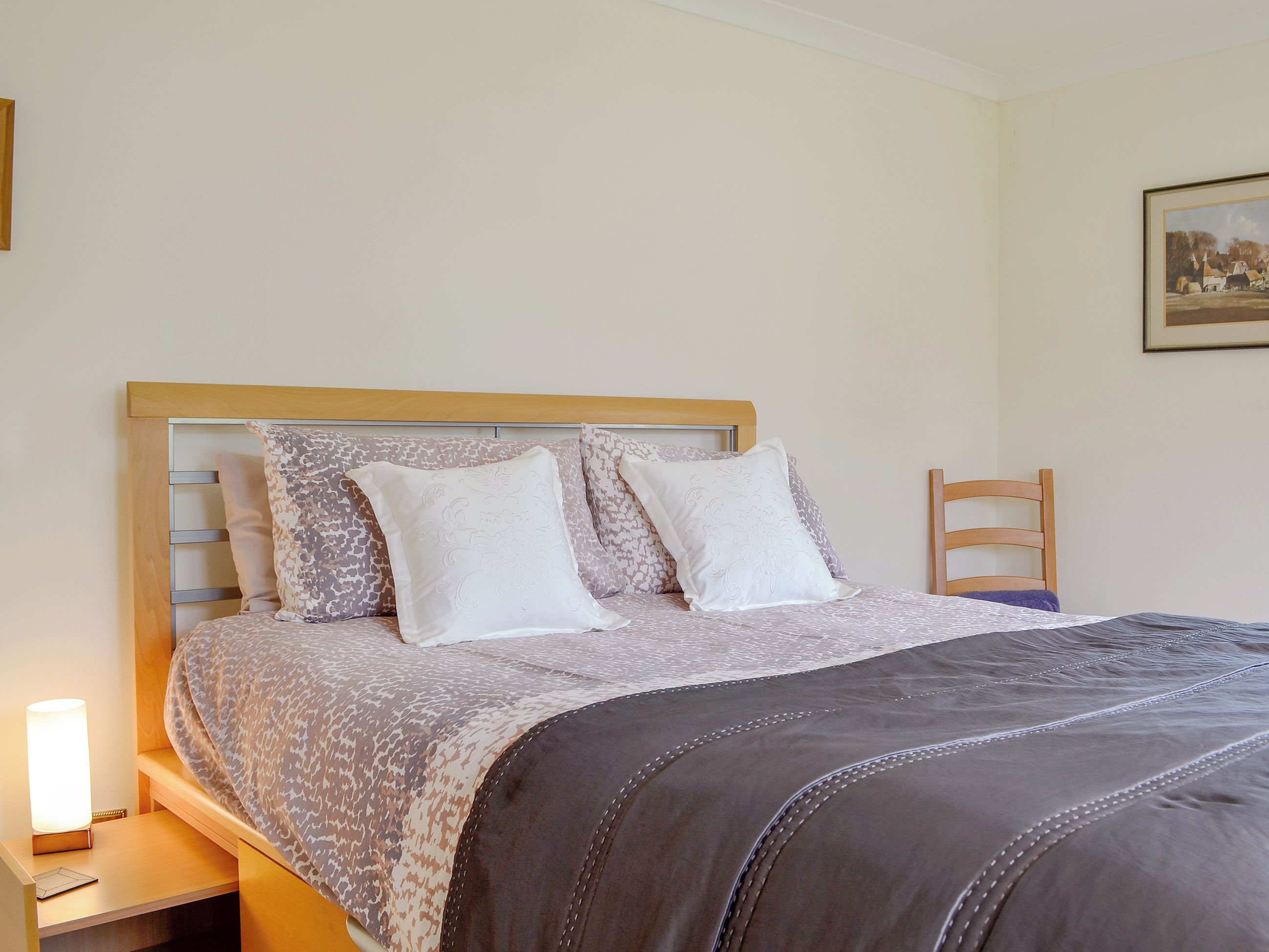 A neatly made bed with patterned bedding, a bedside lamp, and a framed picture on the wall.
