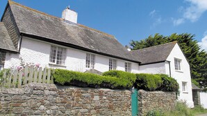 A white building with a stone wall in front, a wooden fence, and a green gate.