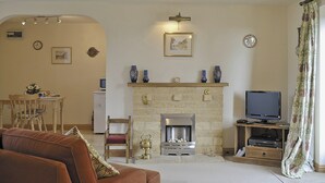 A living room with a fireplace, a television, and a dining area with chairs and a table. - 1 bedroom accommodation in Ebrington, near Chipping Campden (Ebrington, near Chipping Campden)