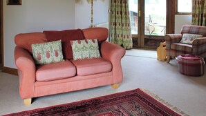 A living room with a red sofa, patterned cushions, a floor lamp, a plaid armchair, and a red patterned rug. - 1 bedroom accommodation in Ebrington, near Chipping Campden (Ebrington, near Chipping Campden)