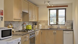 A kitchen with wooden cabinets, a microwave, a stove, a sink, and a dishwasher. - 1 bedroom accommodation in Ebrington, near Chipping Campden (Ebrington, near Chipping Campden)