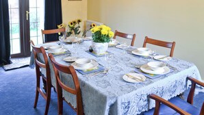 Zona pranzo con tavolo apparecchiato per quattro, sedie, un vaso di girasoli e un lampadario a parete.