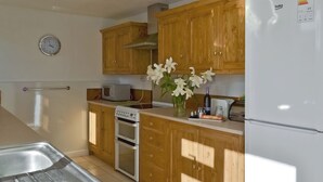 Una cucina con mobili in legno, forno a incasso, microonde e frigorifero.