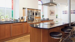 A modern kitchen with a central island, stainless steel appliances, wooden cabinets, and a large window with stained glass.