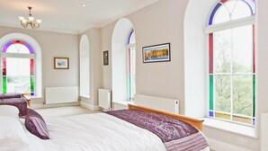 A bedroom with a large bed, arched windows, and a chandelier.