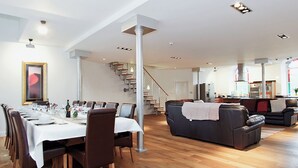 A spacious living area with a dining table set for six, a staircase, and a kitchen in the background.