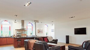 A spacious living area with a kitchen, leather sofas, and a flat-screen TV.