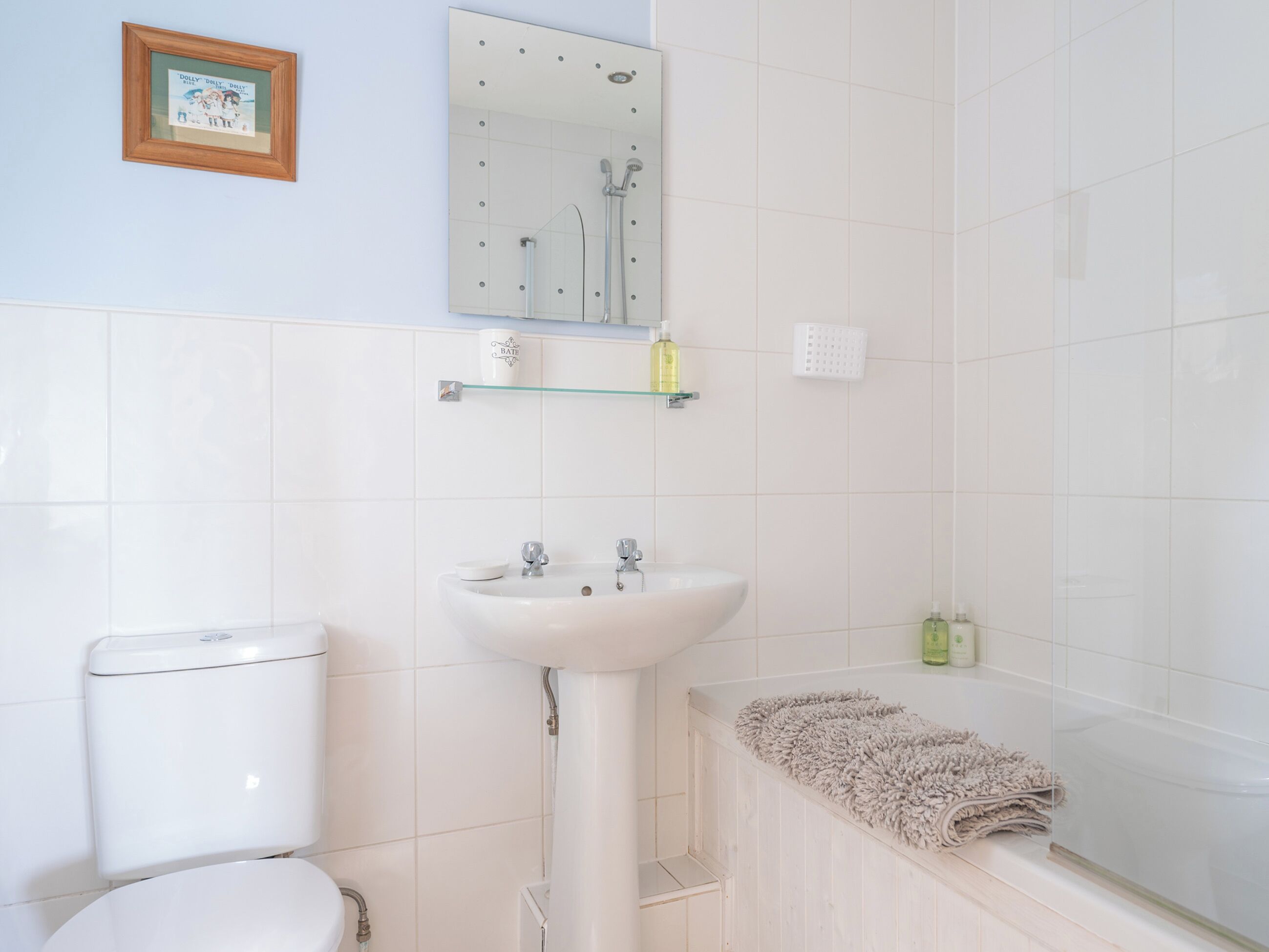 A bathroom with a toilet, sink, and shower. There is a framed picture on the wall and a towel rack.