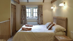 A bedroom with a bed, a nightstand, a window with curtains, and a wall-mounted light fixture.