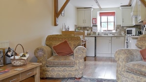 A cozy living room with patterned armchairs, a wooden table, and a kitchen in the background.