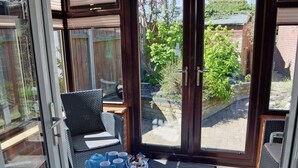 Un invernadero con puerta de cristal, muebles de mimbre y una mesa con tazas azules y una tetera.