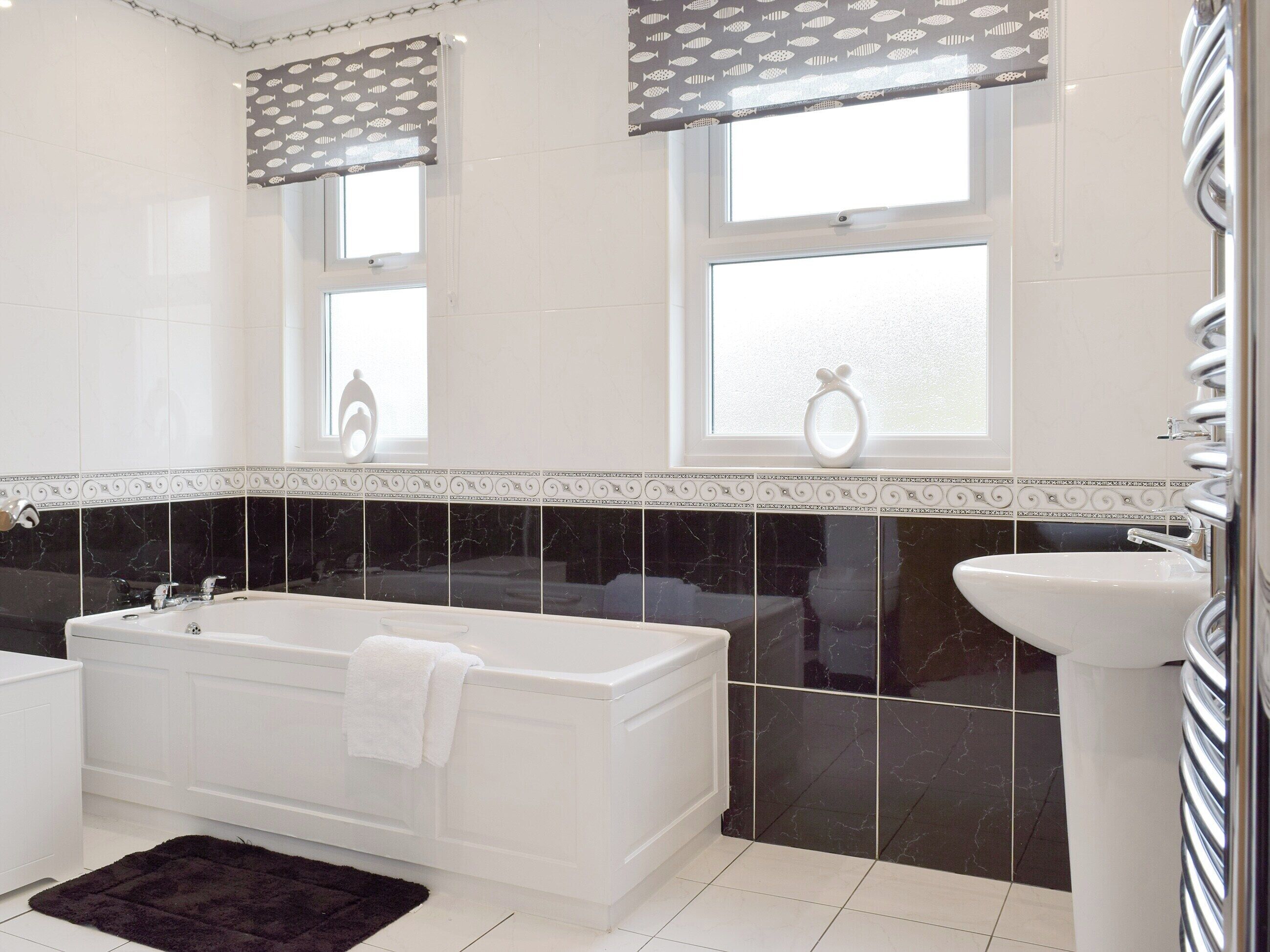 A bathroom with a bathtub, a sink, and two windows with curtains.