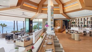 A spacious, modern hotel lobby with a long reception desk, comfortable seating areas, and a view of the ocean.
