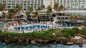 A hotel with multiple swimming pools, palm trees, and a view of the ocean.
