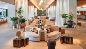 A spacious lobby with multiple seating areas, large potted plants, and a modern chandelier.