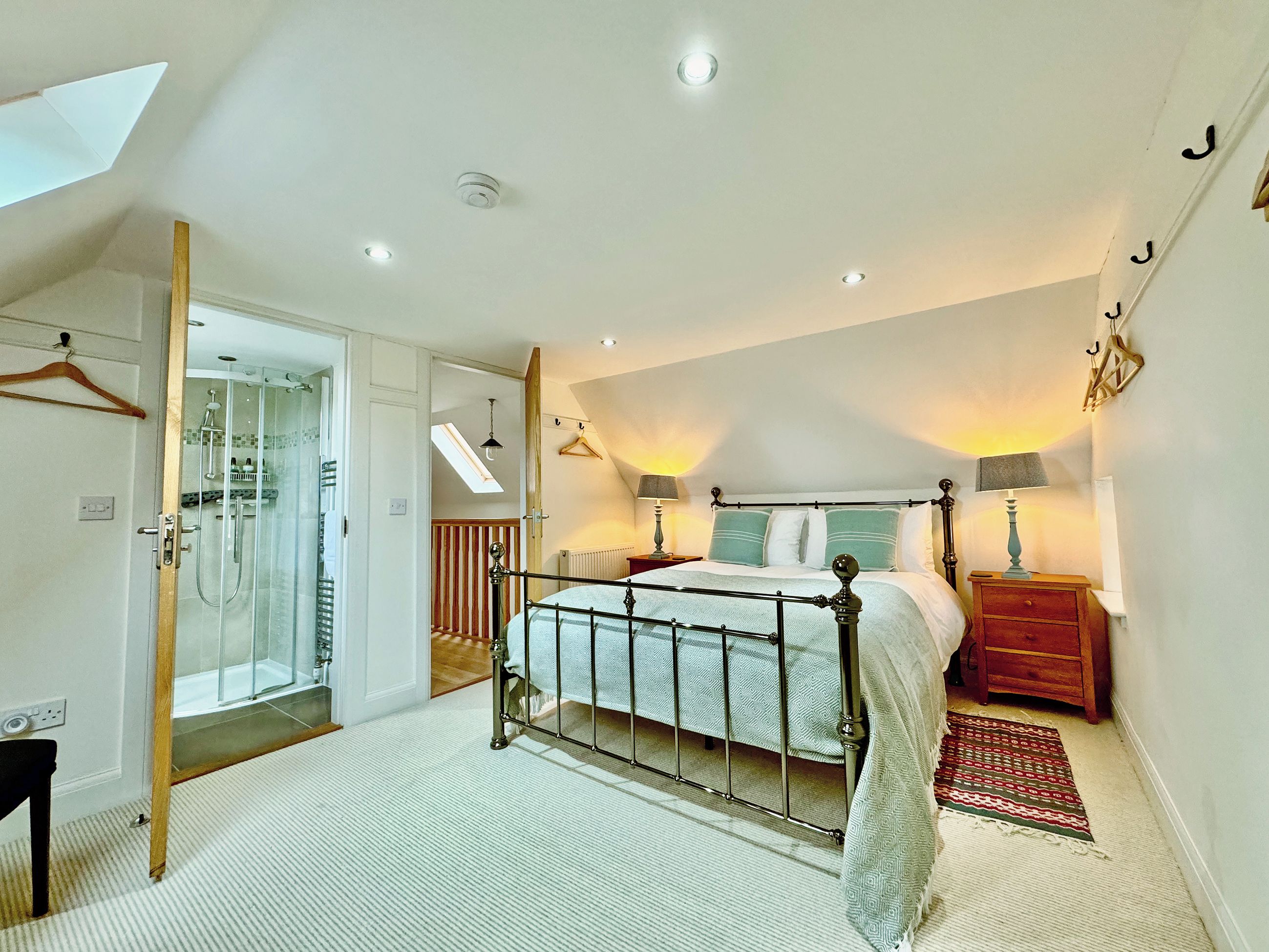 A bedroom with a bed, bedside tables, a hanging light, a radiator, a window, and a door leading to a bathroom.