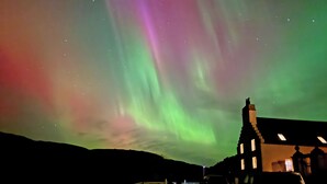 A building with a dark roof and a visible chimney, set against a night sky with the Northern Lights. - 4 bedroom accommodation in Rispond, near Durness (Rispond, near Durness)