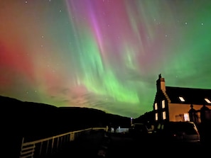 A building with a dark roof and a visible chimney, set against a night sky with the Northern Lights. - 4 bedroom accommodation in Rispond, near Durness (Rispond, near Durness)