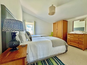 Un dormitorio con cama, cómoda, espejo, lámpara y ventana.