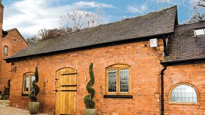 A red brick building with a wooden door and windows, a tiled roof, and a paved walkway. - Groom's Cottage - E5398 (Dunstall Cross, near Barton-under-Needwood)