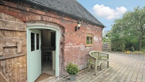 A brick building with a wooden door and a small window. There is a bench and a potted plant outside. - Groom's Cottage - E5398 (Dunstall Cross, near Barton-under-Needwood)