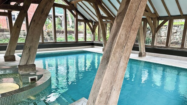 A pool area with a wooden deck, clear blue water, and a stone wall in the background. - Groom's Cottage - E5398 (Dunstall Cross, near Barton-under-Needwood)