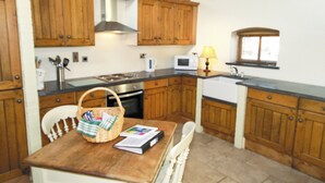 A kitchen with wooden cabinets, a stove, a microwave, and a window. - Groom's Cottage - E5398 (Dunstall Cross, near Barton-under-Needwood)