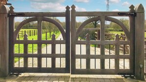A wooden gate with a metal latch, leading to a paved path and a green field. - Groom's Cottage - E5398 (Dunstall Cross, near Barton-under-Needwood)
