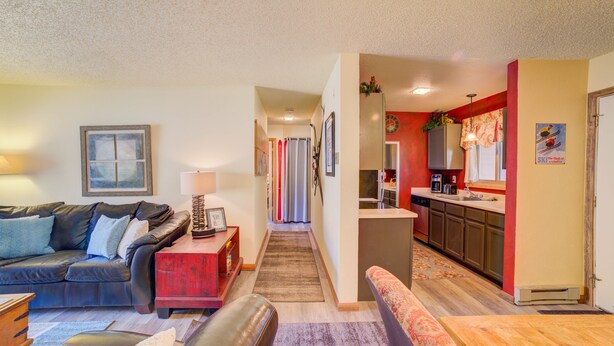 A living room with a sofa, a coffee table, and a red ottoman. There is a hallway leading to a kitchen area with a refrigerator and a sink. - Affordable, updated, quiet, location, location, location! (steamboat springs)