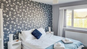 A neatly made bed with white bedding and a blue pillow, a bedside table with a lamp, and a window with curtains. - 2 bedroom accommodation in Beadnell, near Seahouses (Beadnell, near Seahouses)