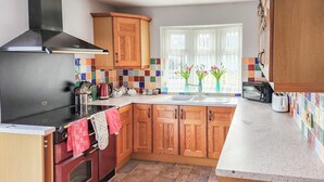 A kitchen with wooden cabinets, a black stove, a microwave, and a window with flowers. - 2 bedroom accommodation in Beadnell, near Seahouses (Beadnell, near Seahouses)