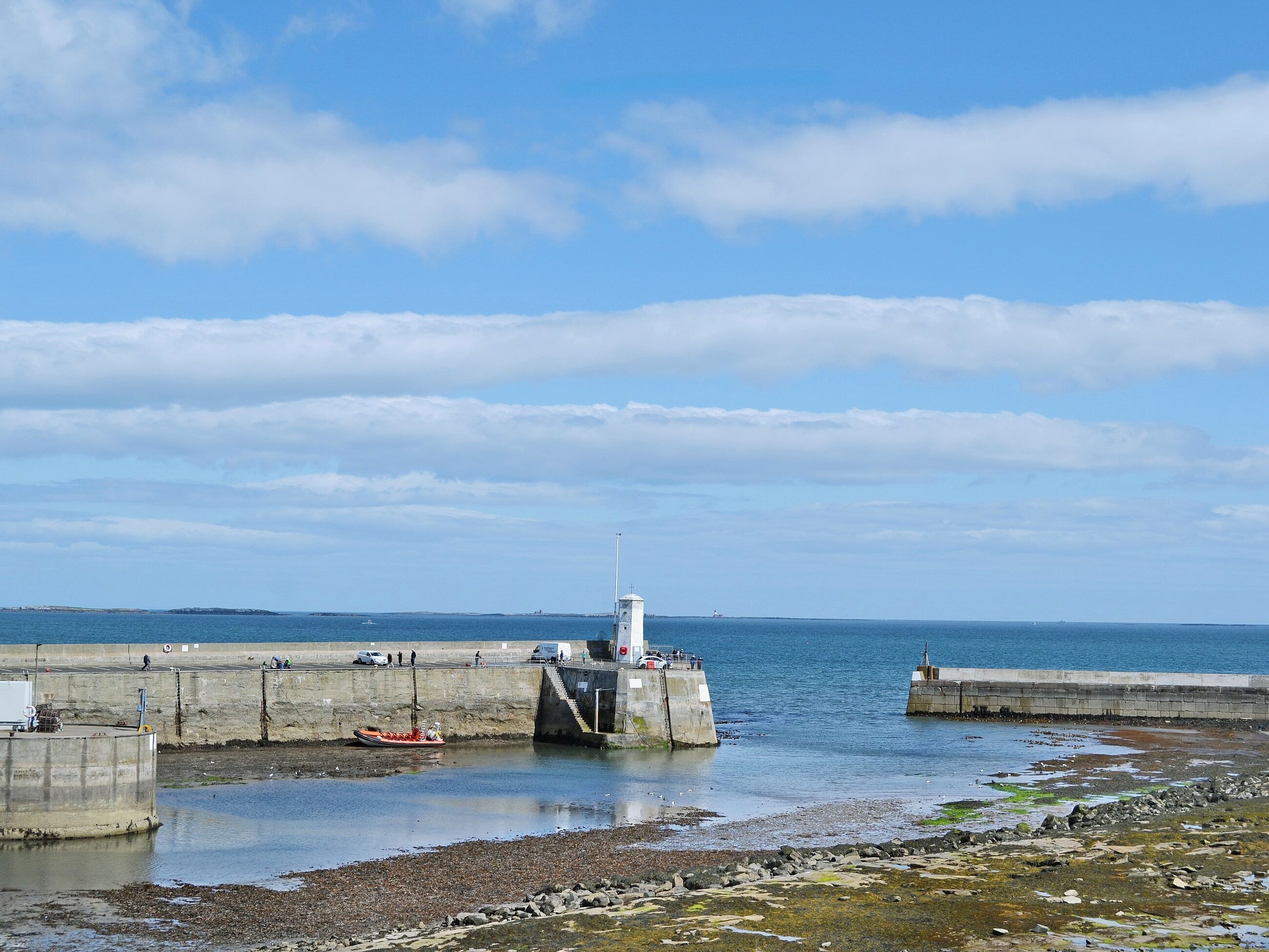 A coastal pier with a lighthouse, concrete structures, and calm water.
