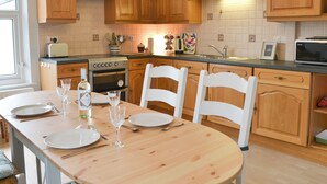 A kitchen with wooden cabinets, a stove, a microwave, and a dining table set for four. - 2 bedroom accommodation in Bassenthwaite, near Keswick (Bassenthwaite, near Keswick)